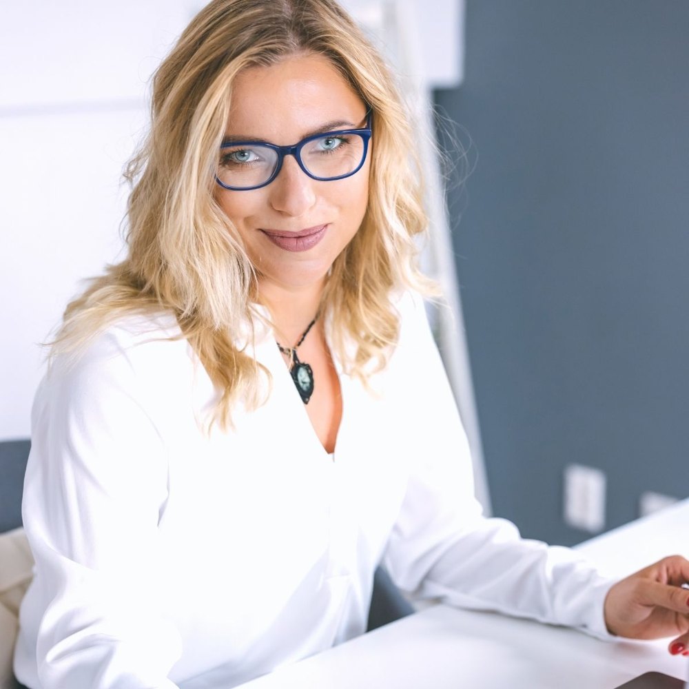 Ania Barańska przy biurku, uśmiechnięta, w okularach